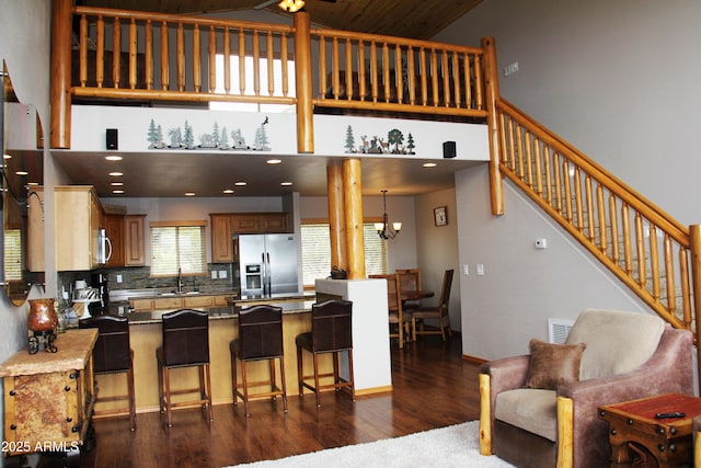 kitchen featuring dark wood finished floors, a kitchen bar, a peninsula, a towering ceiling, and stainless steel appliances