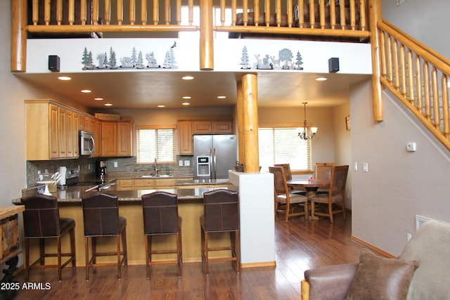 kitchen featuring a peninsula, a sink, stainless steel appliances, a breakfast bar area, and dark wood-style floors