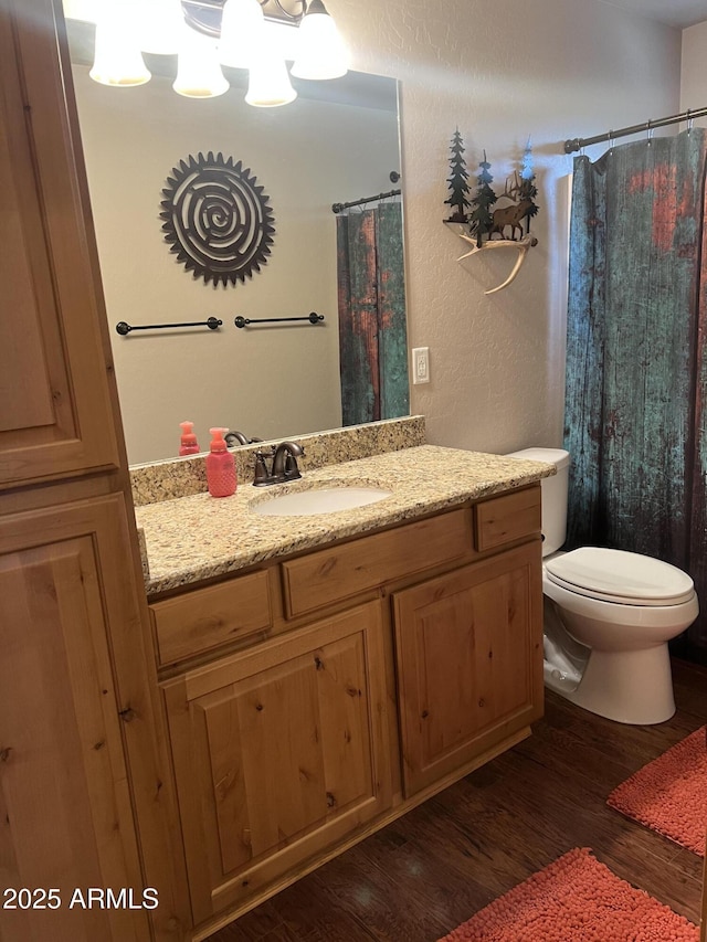 bathroom with a textured wall, toilet, vanity, and wood finished floors