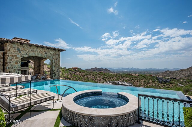 view of swimming pool featuring exterior fireplace, a mountain view, a patio, and an in ground hot tub