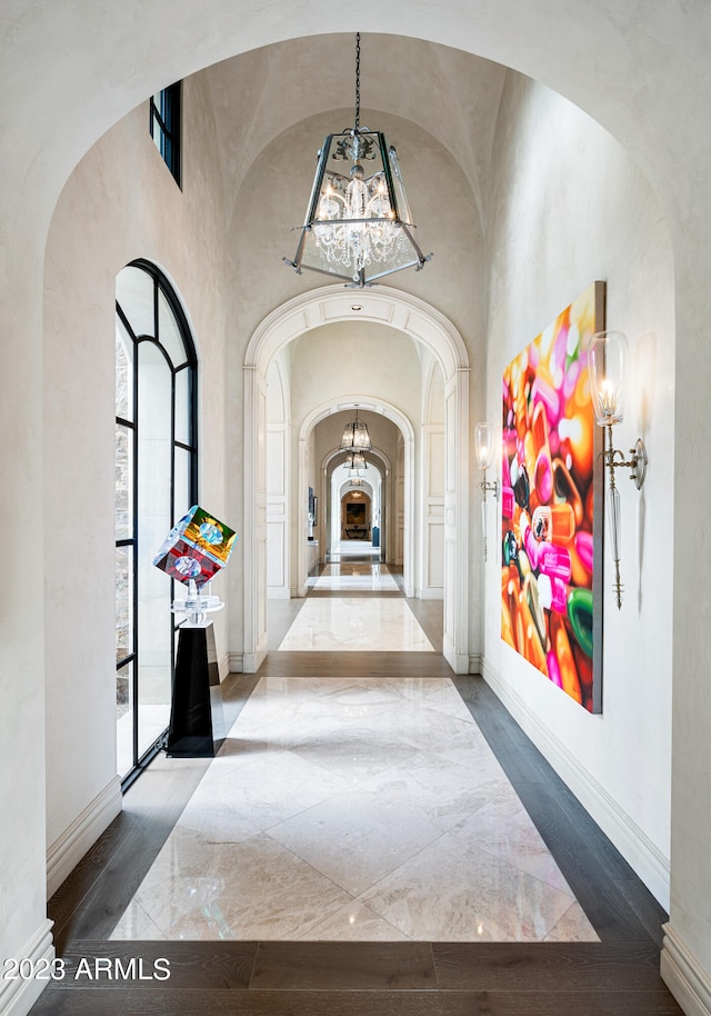 corridor with a notable chandelier, hardwood / wood-style floors, and vaulted ceiling