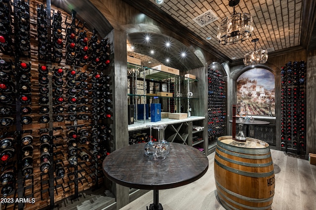 wine cellar with vaulted ceiling, wood-type flooring, an inviting chandelier, ornamental molding, and brick ceiling