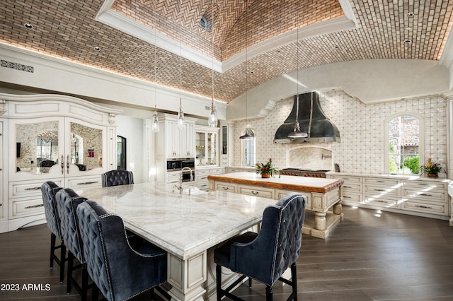 kitchen with wall chimney exhaust hood, high vaulted ceiling, a center island with sink, and hanging light fixtures