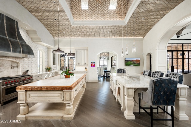 kitchen featuring pendant lighting, range with two ovens, a center island with sink, and a high ceiling