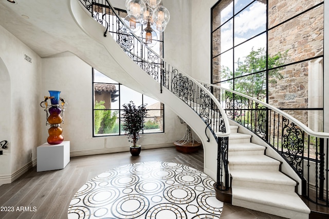 stairway with an inviting chandelier, hardwood / wood-style flooring, and a towering ceiling