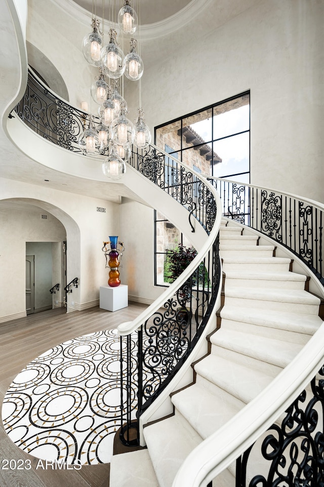 stairs with a raised ceiling, a high ceiling, an inviting chandelier, hardwood / wood-style flooring, and ornamental molding