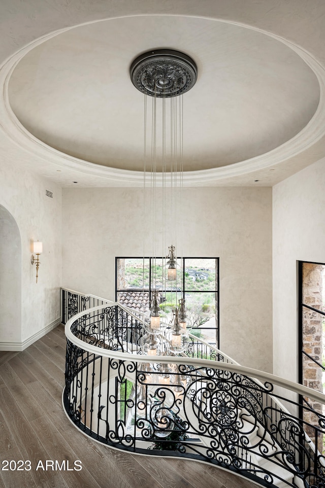 stairs with hardwood / wood-style flooring, a tray ceiling, and a chandelier