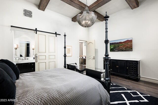 bedroom featuring a barn door, connected bathroom, dark hardwood / wood-style flooring, and beamed ceiling