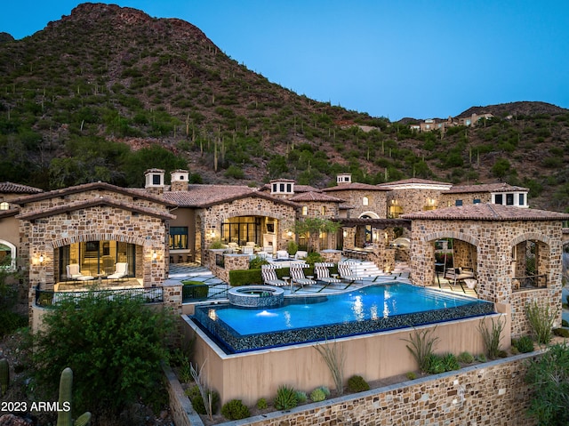 pool at dusk featuring a mountain view, an in ground hot tub, and a patio area