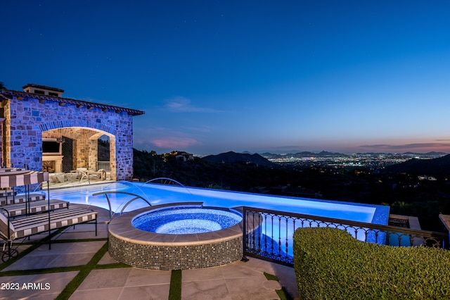 pool at dusk with pool water feature, an in ground hot tub, and a patio area