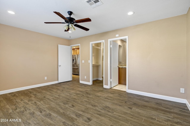 unfurnished bedroom featuring a walk in closet, ceiling fan, dark wood-type flooring, stainless steel fridge with ice dispenser, and a closet