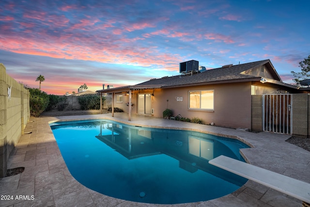 pool at dusk featuring a diving board, a patio area, and central AC