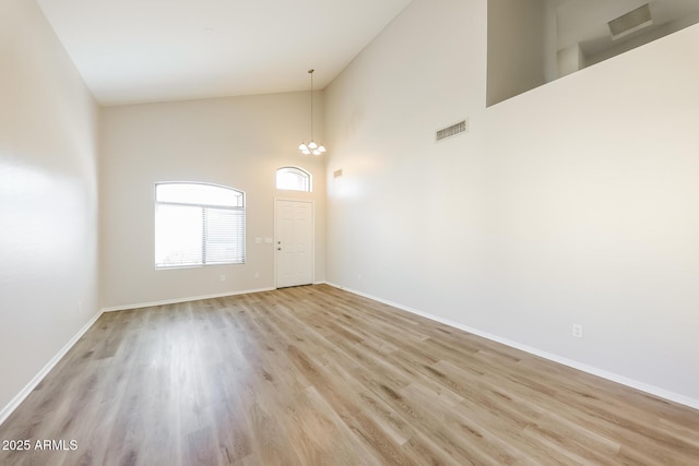 empty room with a high ceiling, an inviting chandelier, and light hardwood / wood-style floors