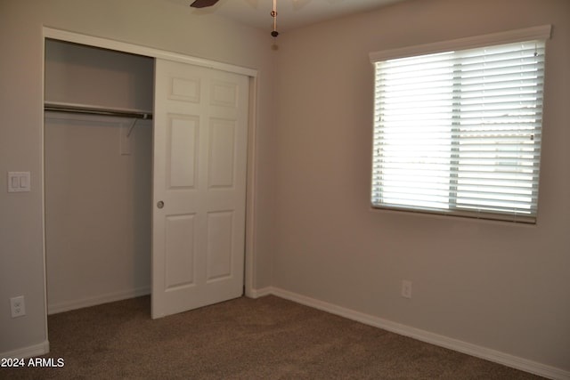 unfurnished bedroom with ceiling fan, a closet, multiple windows, and dark carpet