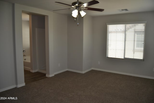 spare room with ceiling fan, a wealth of natural light, and dark colored carpet