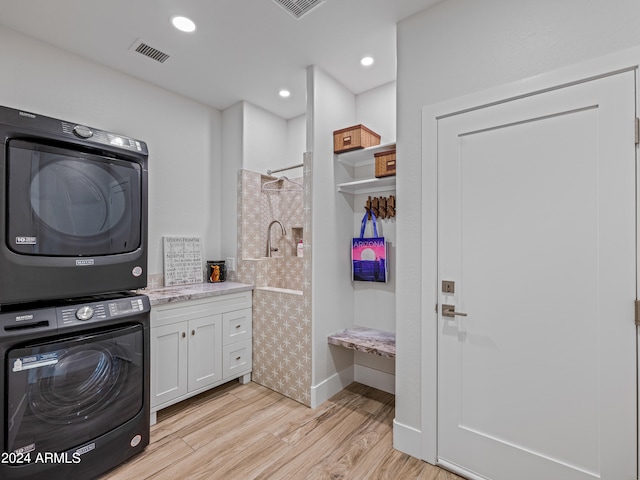 laundry area with light hardwood / wood-style floors, stacked washer / dryer, and cabinets