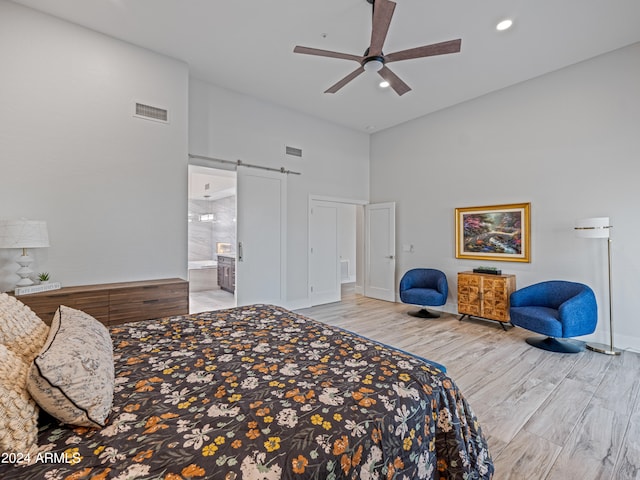 bedroom featuring ceiling fan, a barn door, ensuite bathroom, a towering ceiling, and light hardwood / wood-style floors