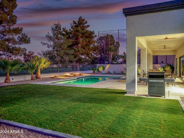 pool at dusk with a patio, ceiling fan, and a yard