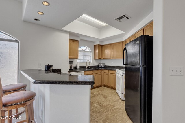 kitchen featuring visible vents, a kitchen breakfast bar, a peninsula, white appliances, and a sink