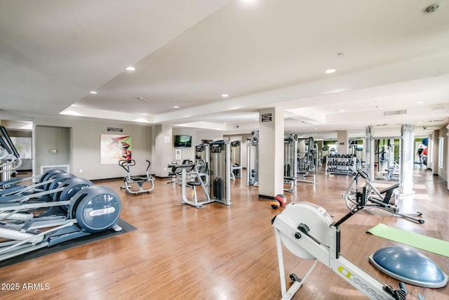 gym with a raised ceiling, light wood-style floors, and recessed lighting