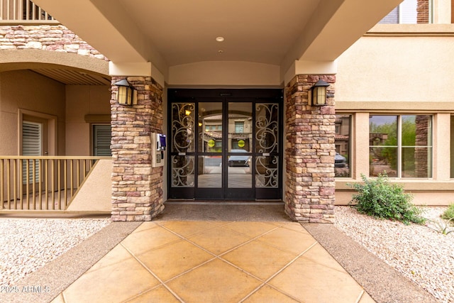 entrance to property featuring stucco siding, stone siding, and french doors