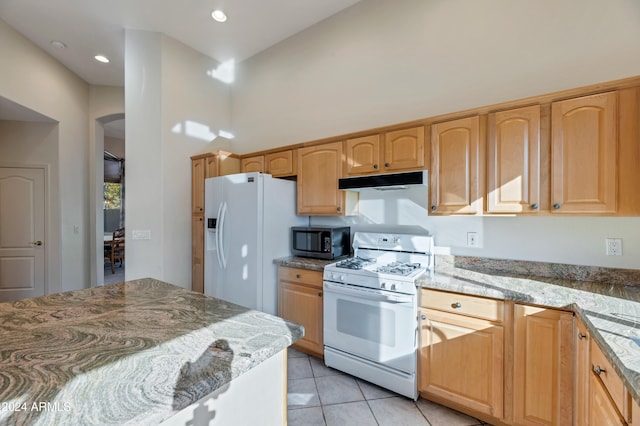 kitchen with light tile patterned floors, white appliances, light stone counters, and light brown cabinets