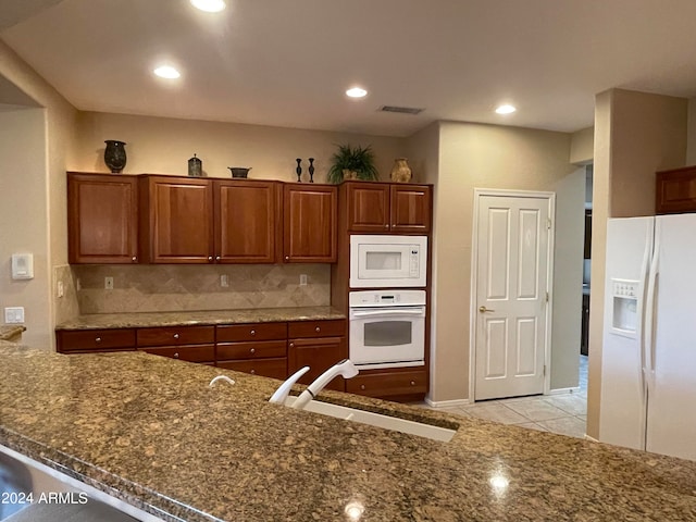 kitchen with tasteful backsplash, light tile patterned floors, dark stone countertops, sink, and white appliances