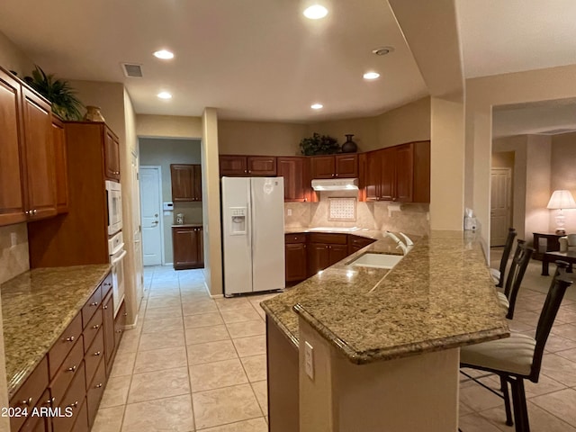 kitchen featuring kitchen peninsula, light tile patterned floors, a kitchen breakfast bar, sink, and white appliances