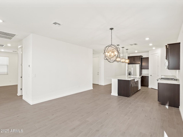 5537 S 246th Ave, Buckeye, AZ 85326 - kitchen with stainless steel appliances, open floor plan, dark brown cabinetry, light countertops, and a chandelier