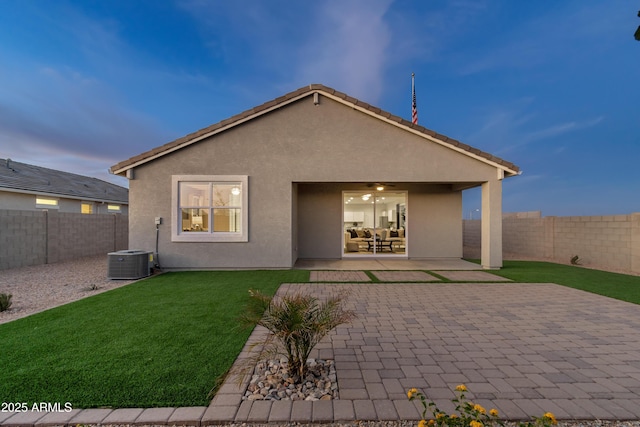 back of property at dusk with a patio, stucco siding, a lawn, a ceiling fan, and a fenced backyard