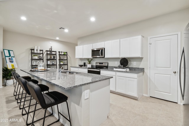 kitchen with visible vents, appliances with stainless steel finishes, light stone countertops, white cabinetry, and a sink
