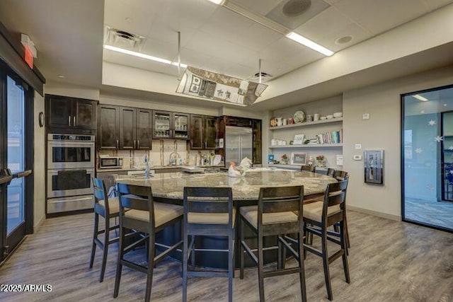 kitchen with appliances with stainless steel finishes, a large island, a breakfast bar, light hardwood / wood-style flooring, and dark brown cabinets