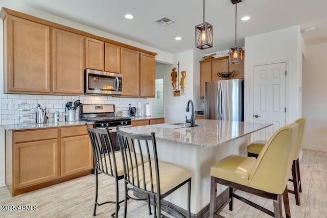 kitchen with sink, light stone counters, a kitchen island with sink, and appliances with stainless steel finishes