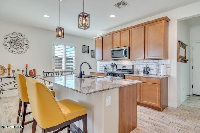 kitchen featuring sink, decorative light fixtures, light stone counters, stove, and decorative backsplash