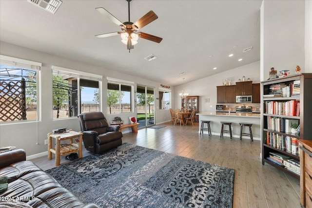 living room featuring ceiling fan with notable chandelier, vaulted ceiling, and light hardwood / wood-style flooring