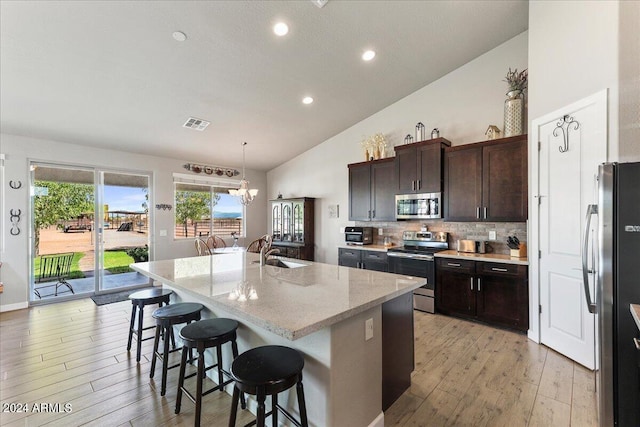 kitchen with a chandelier, light hardwood / wood-style floors, a kitchen island with sink, stainless steel appliances, and decorative light fixtures