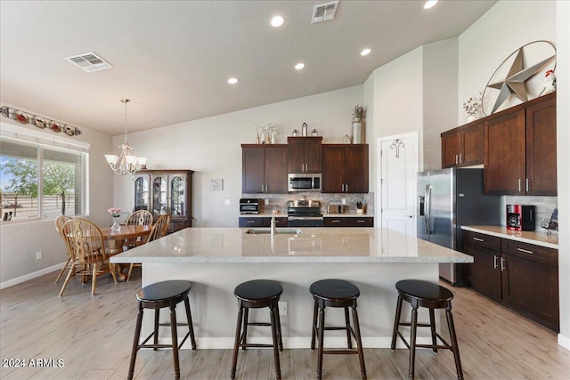 kitchen with an island with sink, appliances with stainless steel finishes, light wood-type flooring, and a chandelier