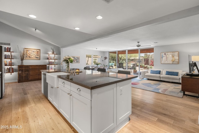 kitchen featuring light wood finished floors, a center island with sink, open floor plan, and a sink