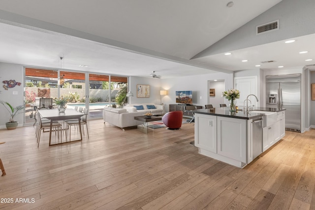 kitchen featuring light wood-style flooring, stainless steel appliances, a sink, visible vents, and dark countertops