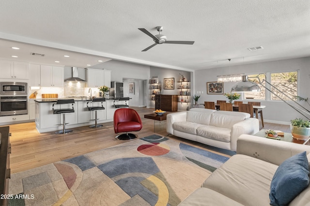 living area with lofted ceiling, recessed lighting, visible vents, light wood-style flooring, and a textured ceiling