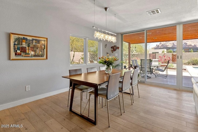 dining area featuring a textured ceiling, visible vents, baseboards, light wood-style floors, and a wall of windows