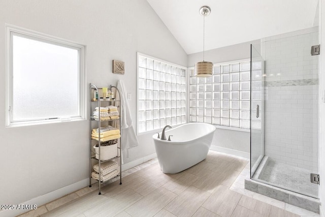 bathroom featuring lofted ceiling, a freestanding tub, a shower stall, and baseboards