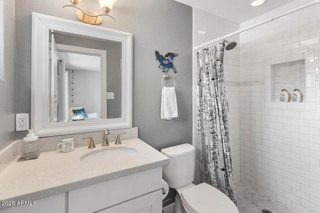 full bath featuring a stall shower, a textured wall, vanity, and toilet