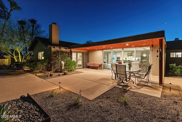 back of house at night with a patio area and a chimney