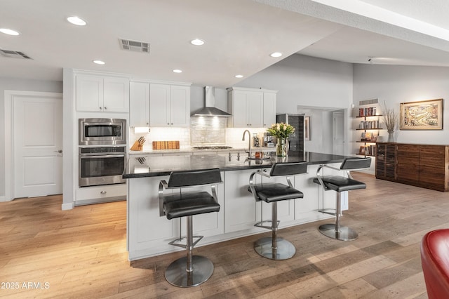 kitchen with stainless steel appliances, lofted ceiling, visible vents, and wall chimney exhaust hood