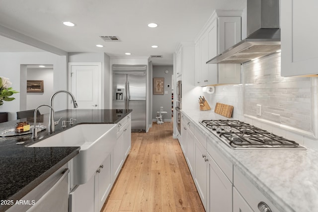 kitchen with visible vents, wall chimney exhaust hood, stainless steel appliances, light wood-style floors, and white cabinetry