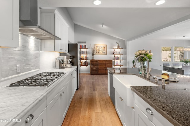 kitchen featuring light wood finished floors, lofted ceiling, wall chimney range hood, stainless steel gas cooktop, and a sink