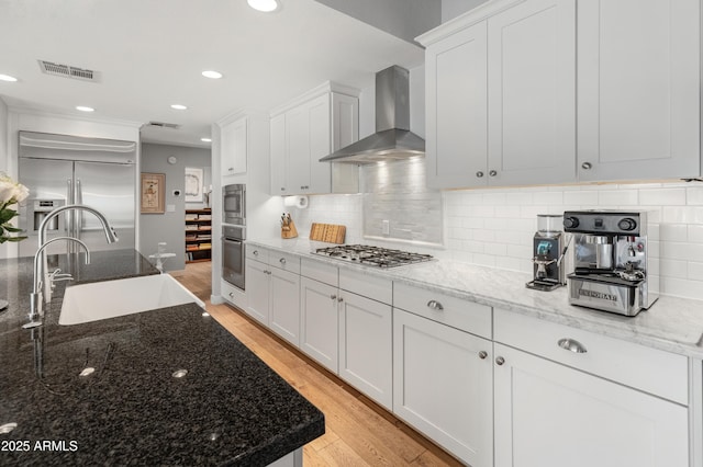 kitchen featuring light wood finished floors, visible vents, appliances with stainless steel finishes, wall chimney range hood, and a sink