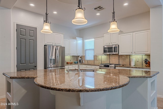 kitchen featuring stainless steel appliances, a large island with sink, hanging light fixtures, sink, and white cabinets