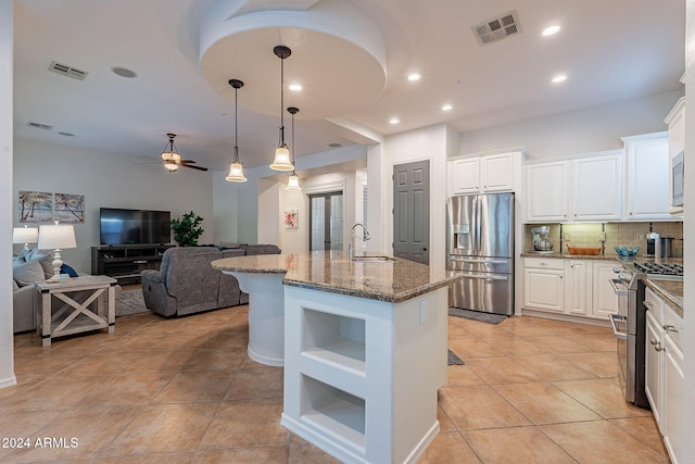 kitchen featuring stainless steel appliances, backsplash, white cabinetry, stone counters, and an island with sink